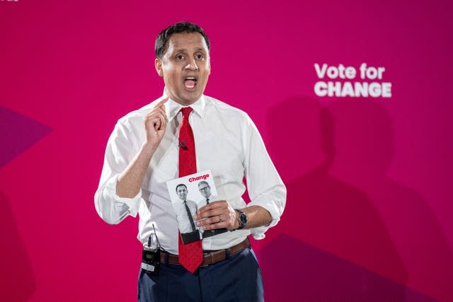 Anas Sarwar speaking, with hand raised, in front of Labour signage