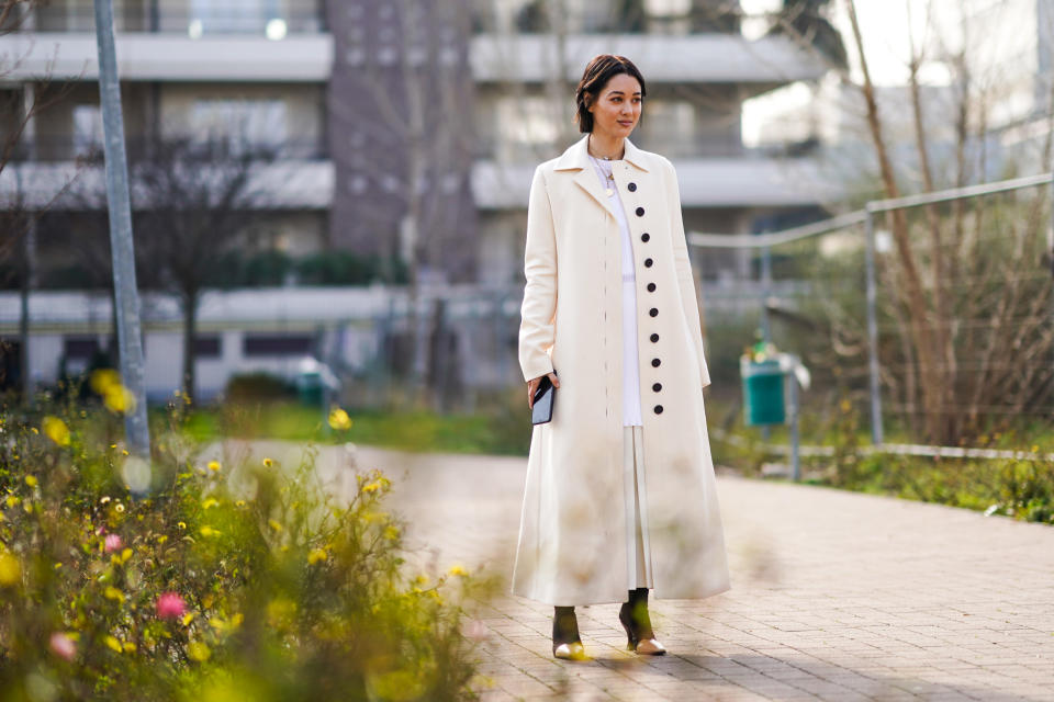 MILAN, ITALY - FEBRUARY 23: A guest wears a necklace, a white long coat with black buttons, boots with metallic parts, a white dress, outside BOSS, during Milan Fashion Week Fall/Winter 2020-2021 on February 23, 2020 in Milan, Italy. (Photo by Edward Berthelot/Getty Images)