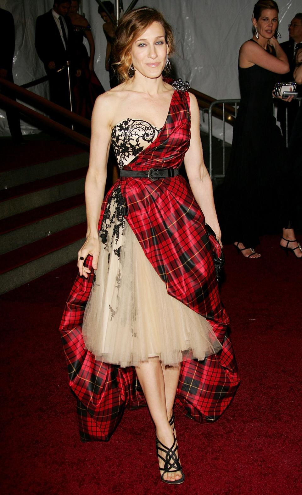 A woman in a tartan and lace asymmetrical gown poses on a staircase at an event