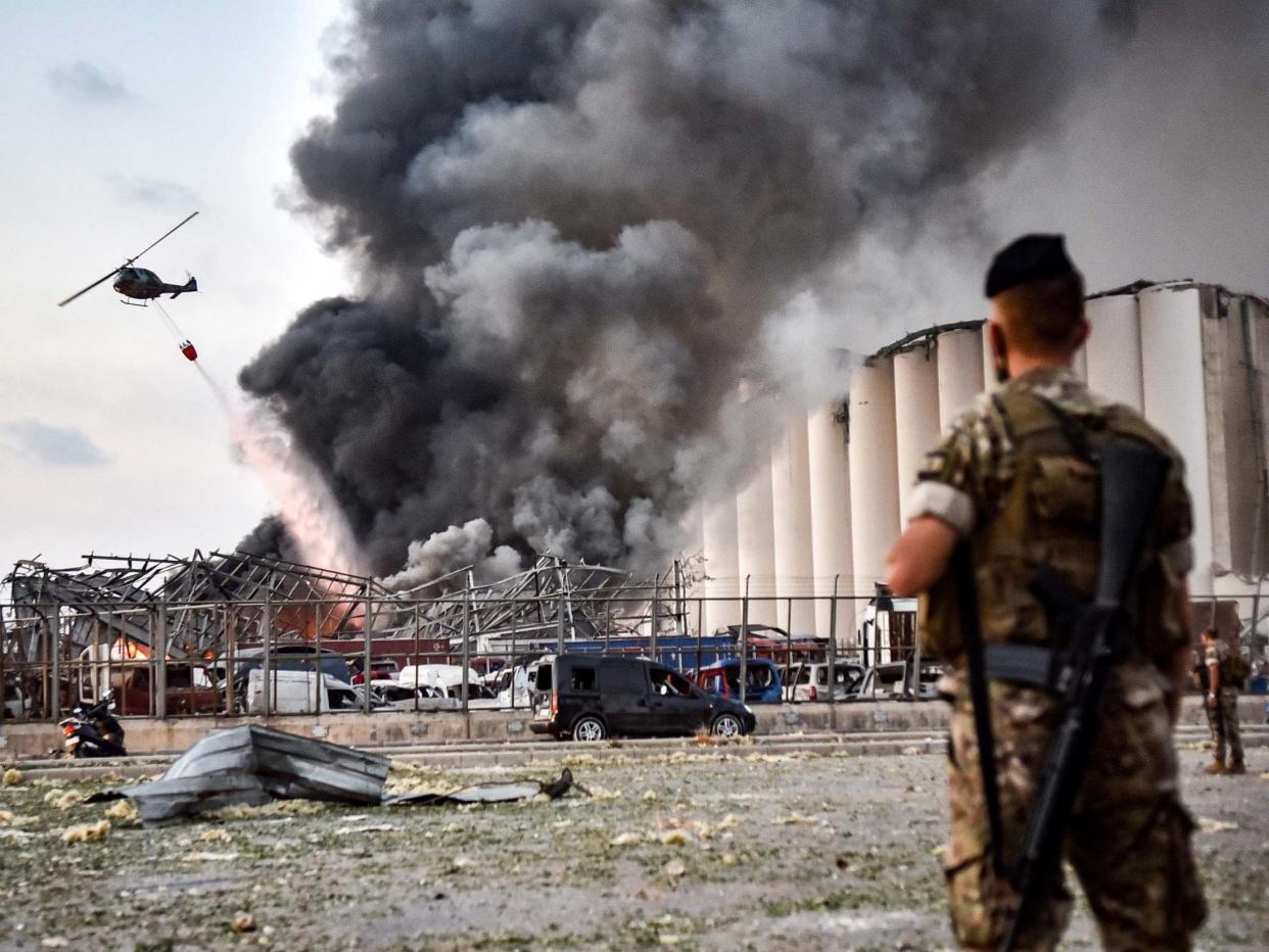 Lebanese army soldiers stand while behind a helicopter puts out a fire at the scene of an explosion at the port of Lebanon's capital Beirut: AFP via Getty Images