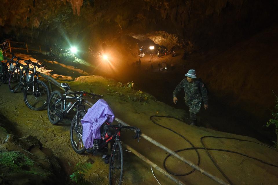 <p>The abandoned bicycles belonging to a missing Thai soccer team are seen parked together while Thai rescue personnel conduct rescue operations under floodlights, seen in the background, at the entrance of Tham Luang cave in Chiang Rai province on June 26, 2018 as the search continues for the 12 children and their coach. (Photo from Lillian Suwanrumpha/AFP/Getty Images) </p>