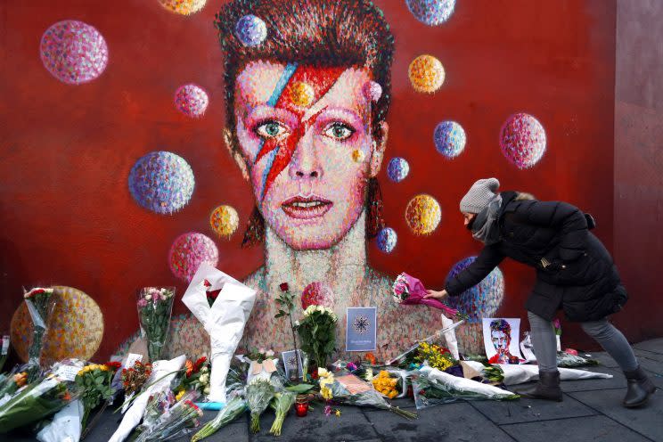 <i>[A woman leaves flowers beneath a mural of David Bowie in Brixton on January 11, 2016 in London, England. British music and fashion icon David Bowie died earlier today at the age of 69 after a battle with cancer. (Carl Court/Getty Images)]</i>