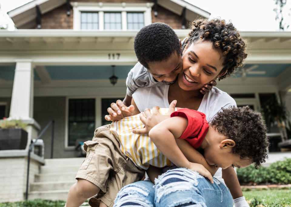 Mother playing with two young children in front of a house