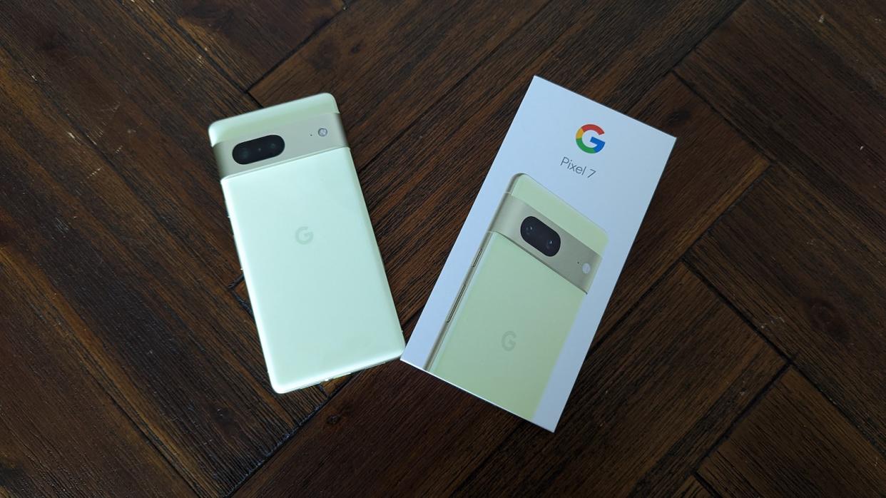 A yellow Google Pixel 7 with its packaging on a brown table.