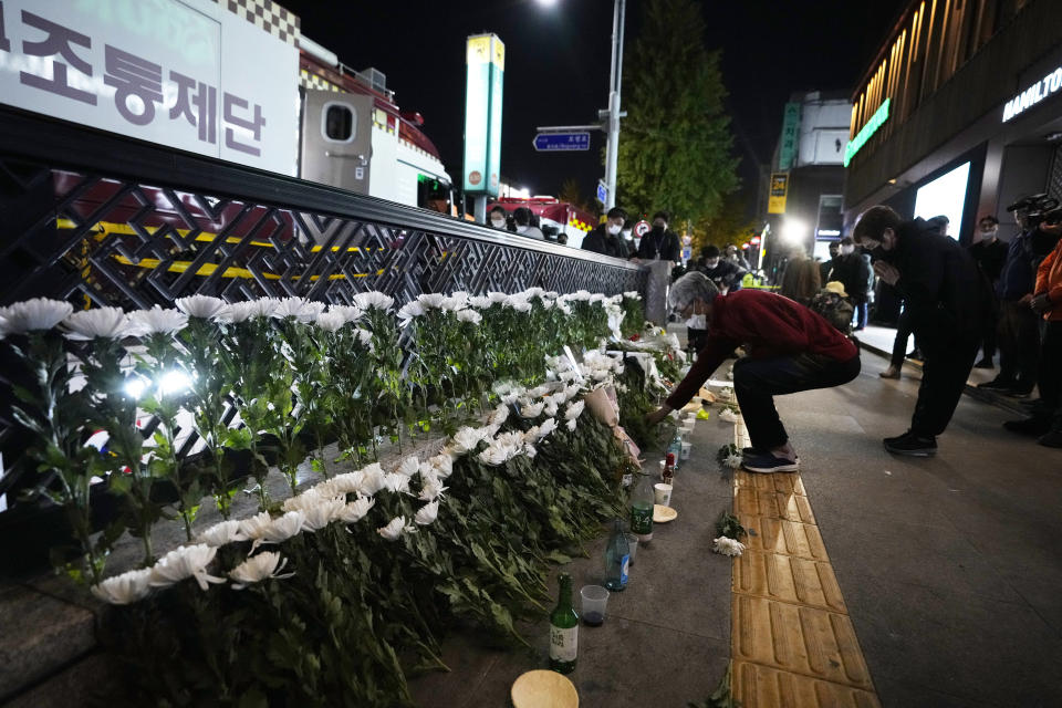 A woman places flowers to pay tribute for victims near the scene of a deadly accident in Seoul, South Korea, Sunday, Oct. 30, 2022, following Saturday night's Halloween festivities. A mass of mostly young people among tens of thousands who gathered to celebrate Halloween in Seoul became trapped and crushed as the crowd surged into a narrow alley, killing dozens of people and injuring dozens of others in South Korea’s worst disaster in years. (AP Photo/Ahn Young-joon)