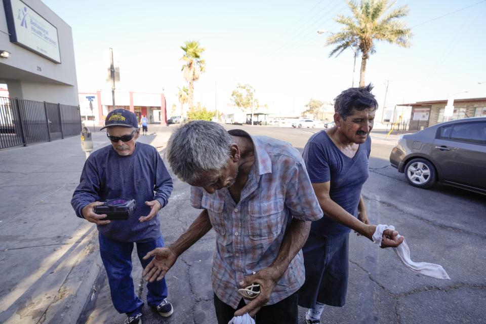 Three men, who are homeless, react as they are given cold, wet towels by Maribel Padilla of the Brown Bag Coalition, Thursday, July 20, 2023, in Calexico, Calif. Once temperatures hit 113 degrees Fahrenheit (45 Celsius), Padilla and the Brown Bag Coalition meet up with people who are homeless in Calexico, providing them with cold, wet towels, and some refreshments to help them endure the scorching temperatures. (AP Photo/Gregory Bull)