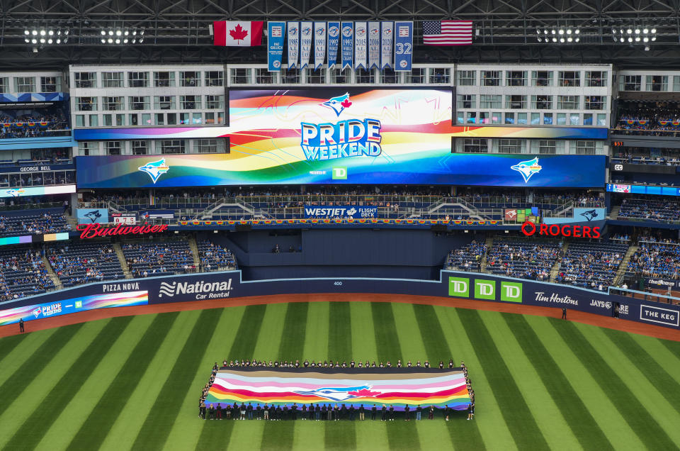 People hold a Pride-themed Toronto Blue Jays flag to celebrate Pride Weekend before the team's baseball game against the Minnesota Twins on Friday, June 9, 2023, in Toronto. (Mark Blinch/The Canadian Press via AP)