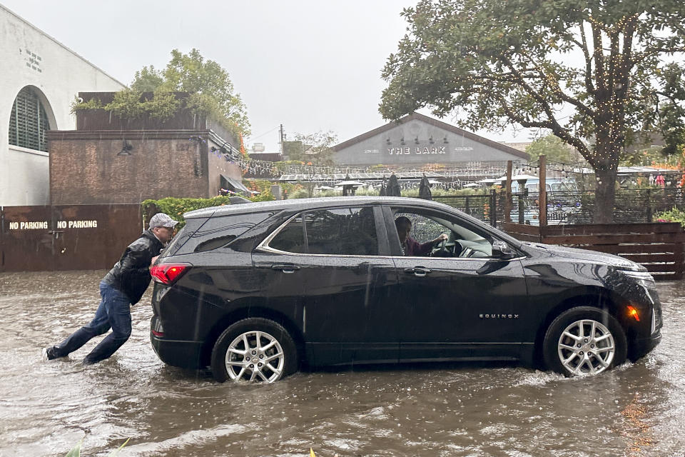 A man tries to push a vehicle out of a flooded street as rain comes down, Thursday, Dec. 21, 2023, in Santa Barbara, Calif. (AP Photo/Eugene Garcia)