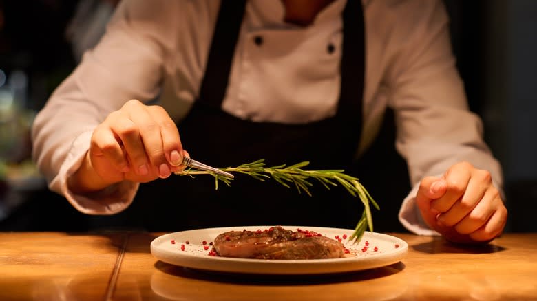 chef placing rosemary on meat