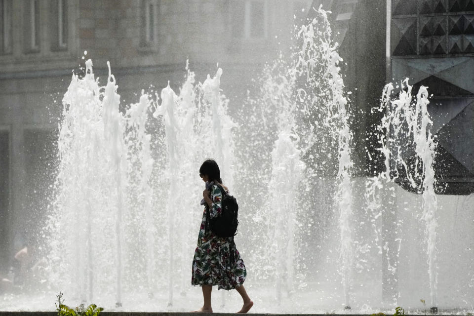 A woman walks past a fountain on a hot summer day in Berlin, Germany, Sunday, June 19, 2022. People flocked to parks and pools across Western Europe on Saturday for a bit of respite from an early heat wave. In Germany, where highs of 38 C (100.4 F) were expected, the health minister urged vulnerable groups to stay hydrated.(AP Photo/Markus Schreiber)