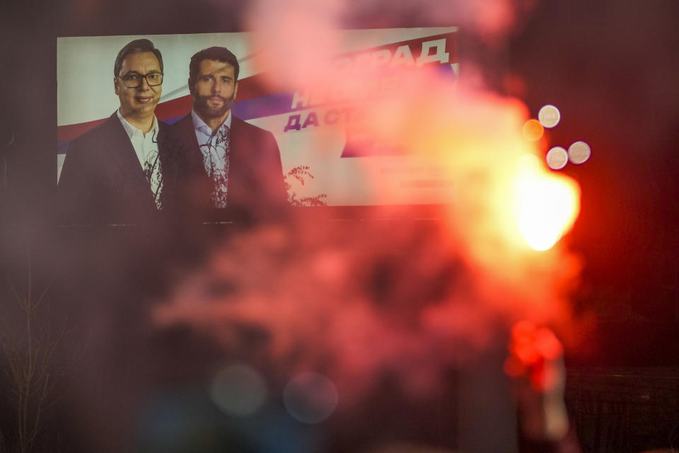 A man holds a flare in front of a pre-election billboard showing Serbian President Aleksandar Vucic, left, and Belgrade mayor candidate Aleksandar Sapic, during a final pre-election rally of opposition "Serbia against violence" coalition in Belgrade, Serbia, Tuesday, Dec. 12, 2023. Serbia's President Vucic is pushing hard to reassert his populist party's dominance at this weekend's early parliamentary and local elections that observers say are being held in an atmosphere of intimidation and media bias. (AP Photo/Darko Vojinovic)