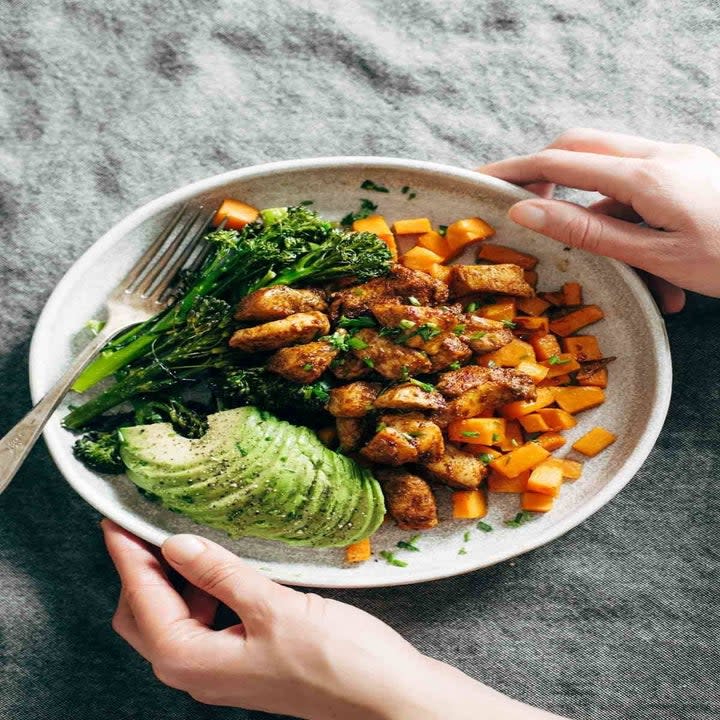 A bowl with sweet potato, chicken, avocado, and broccolini.