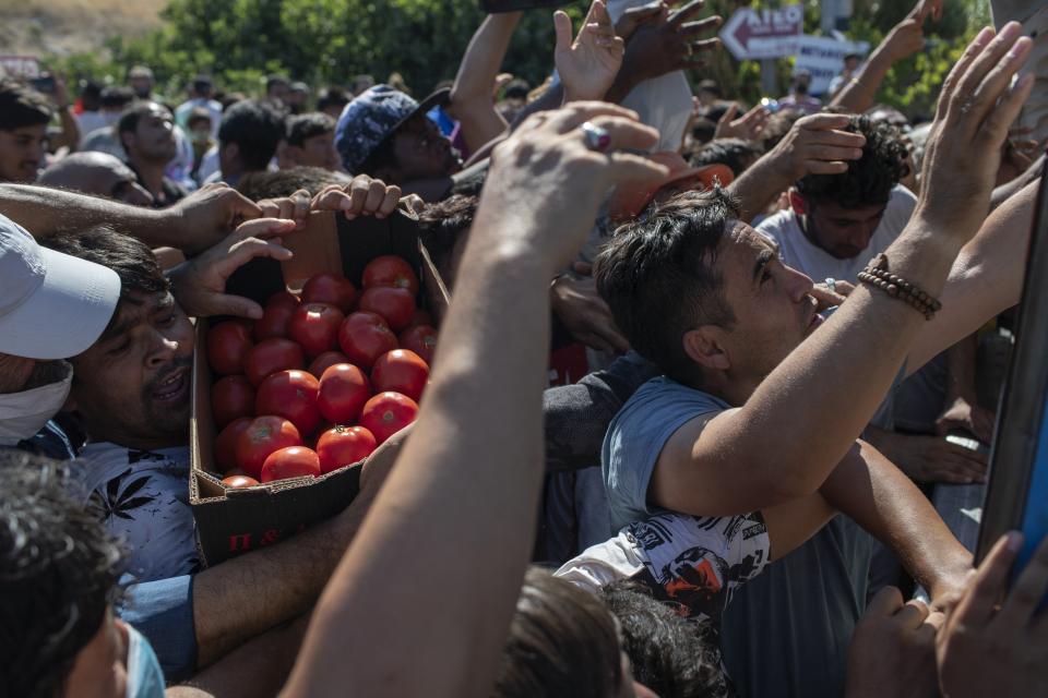 Migrants argue for a crate of tomatoes during a food distribution on the northeastern island of Lesbos, Greece, Thursday, Sept. 10, 2020. Little remained of Greece's notoriously overcrowded Moria refugee camp Thursday after a second fire overnight destroyed nearly everything that had been spared in the original blaze, leaving thousands more people in need of emergency housing. (AP Photo/Petros Giannakouris)