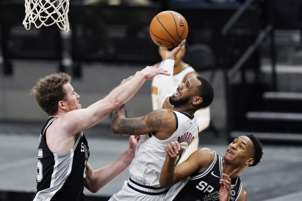 Denver Nuggets guard Monte Morris, center, shoots over San Antonio Spurs center Jakob Poeltl, left, and San Antonio Spurs guard Devin Vassell, right, during the second half of an NBA basketball game in San Antonio, Friday, Jan. 29, 2021. (AP Photo/Eric Gay)