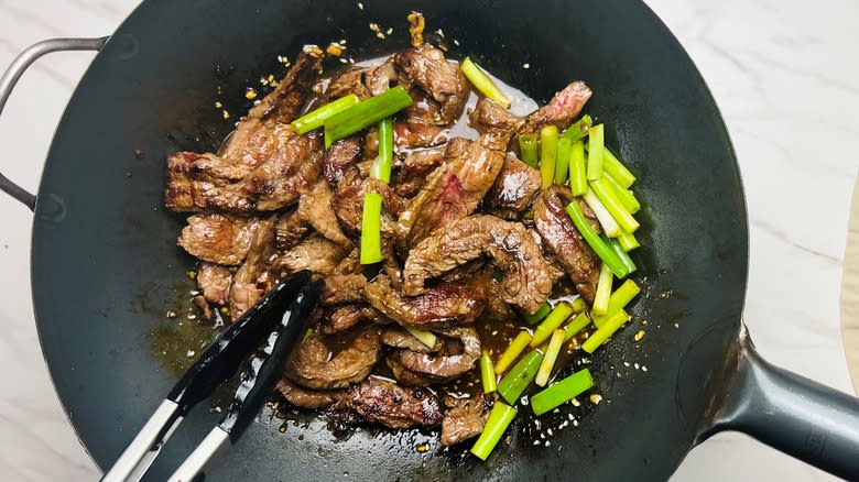 steak strips and green onions in wok