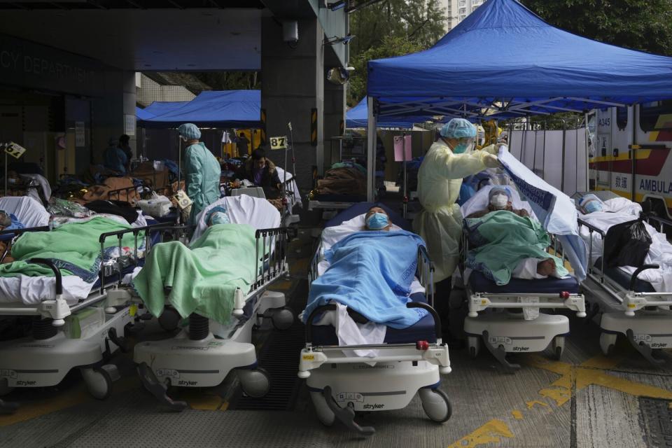 Masked people lie in hospital beds, some under tents, outside a building