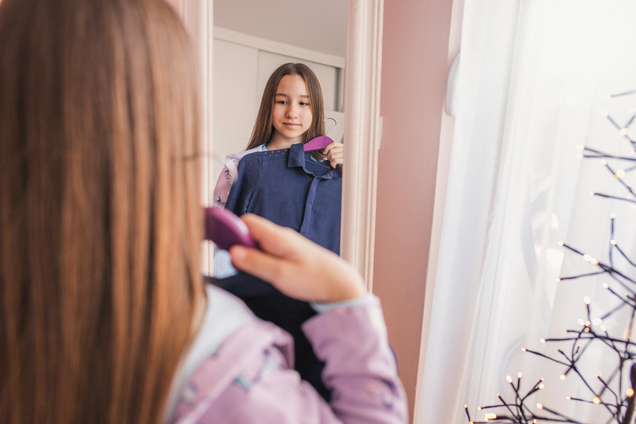 Should parents ask their kids to change? We asked an expert to weigh in on this sensitive topic about clothes. (Getty) Kids change clothes Little girl choosing dresses in white bedroom. Child watching mirror reflection holding pink dress choosing outfit. Girls nursery. Shopping clothing for kids. Dressing room interior for children