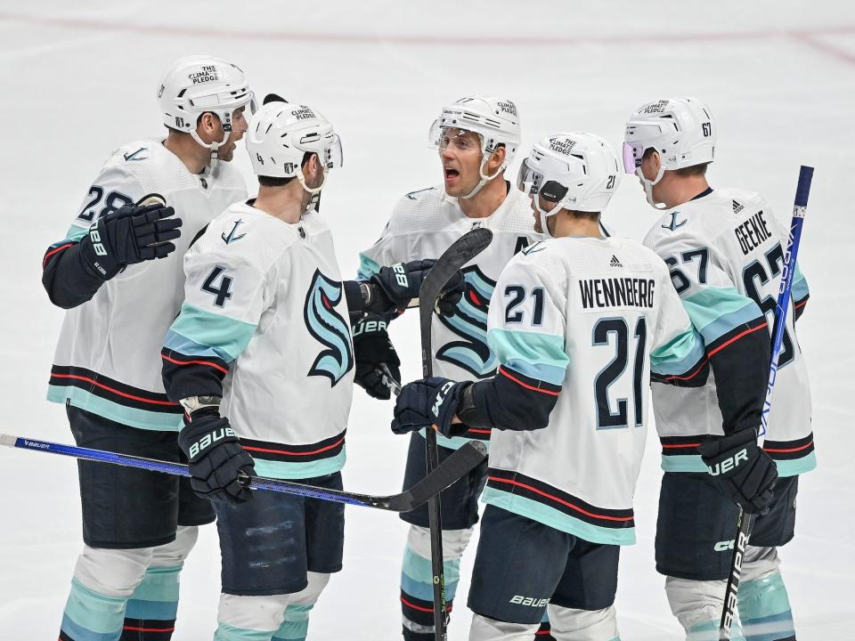 Players from the Seattle Kraken hockey team huddle on the ice.