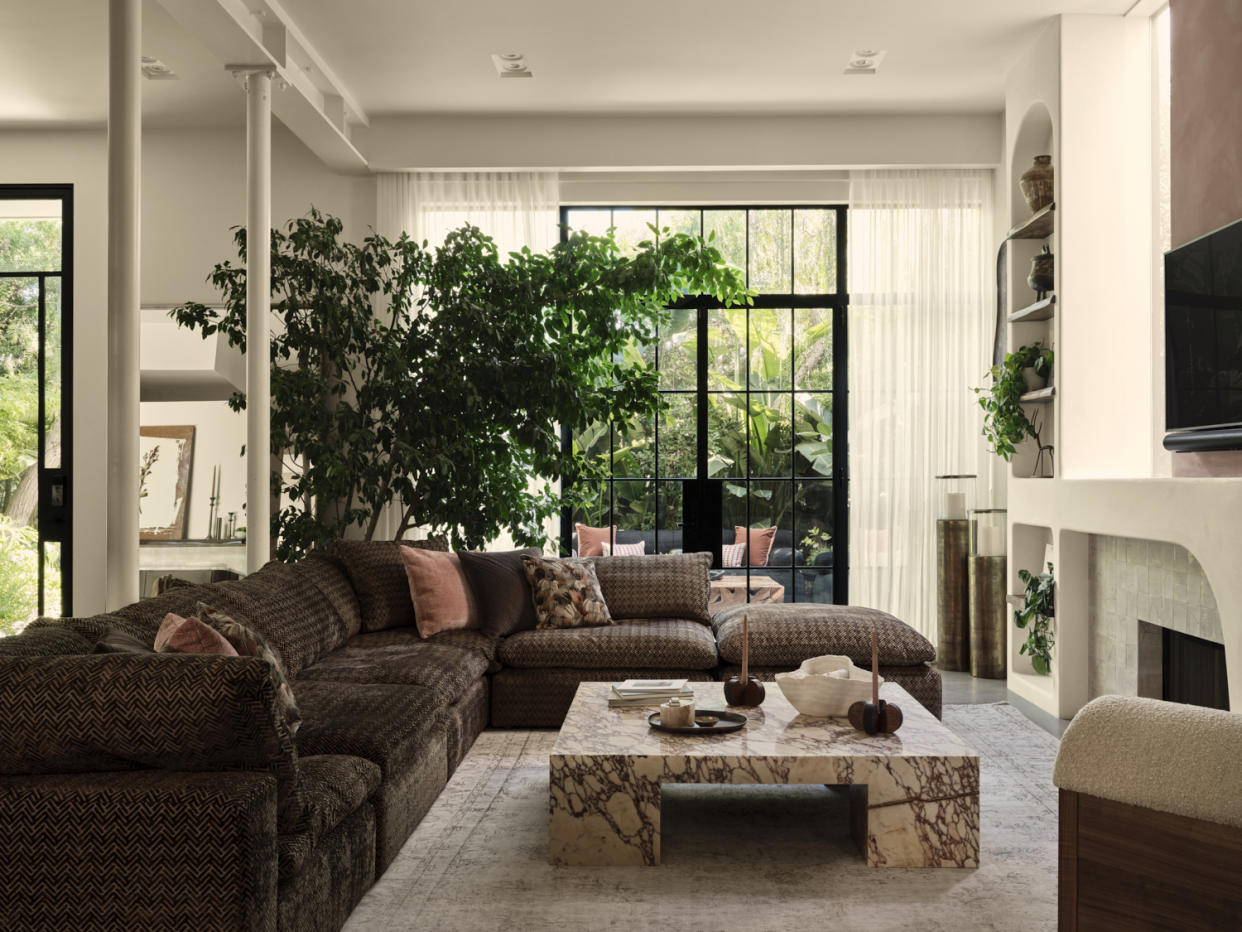  A living room with a brown sofa, a marble coffee table, and a large tree . 