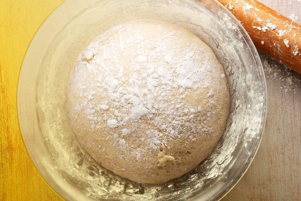 A loaf of bread in a glass bowl with a rolling pin next to it