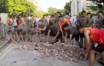 In this image made from video, People’s Liberation Army soldiers, dressed in shorts and T-shirts pick up bricks scattered by protesters at Hong Kong Baptist University in Hong Kong, Saturday, Nov. 16, 2019. Troops from the Chinese army joined an effort to clean up debris outside the university, which was the site of clashes this week. (Television Broadcasts Limited Hong Kong via AP)