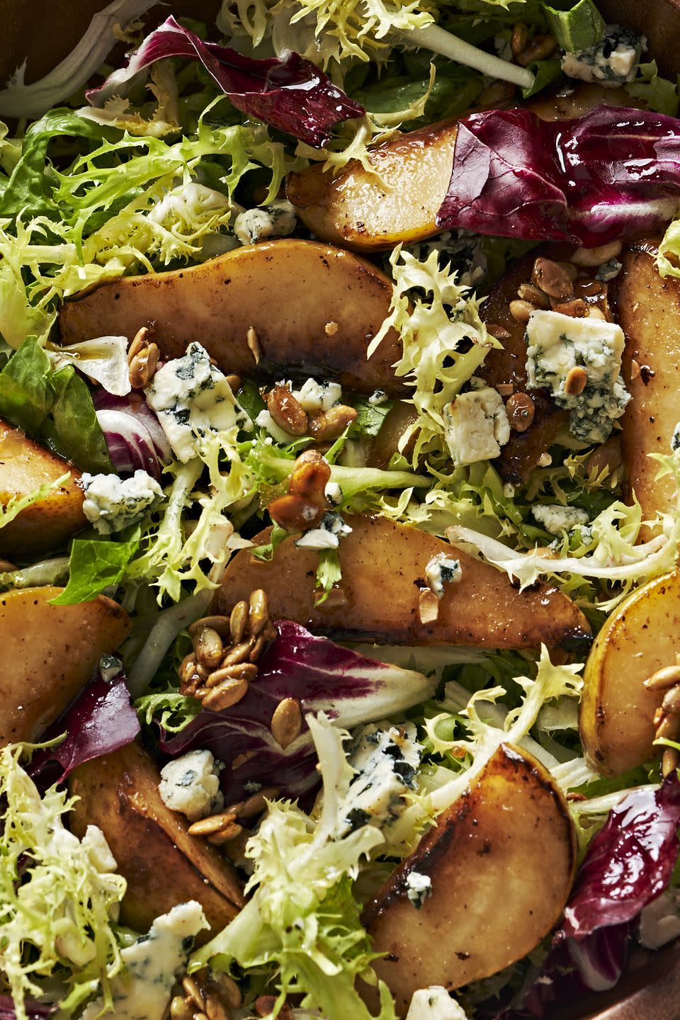 roasted pear salad with mixed greens, candied pepitas, and blue cheese in a wooden bowl