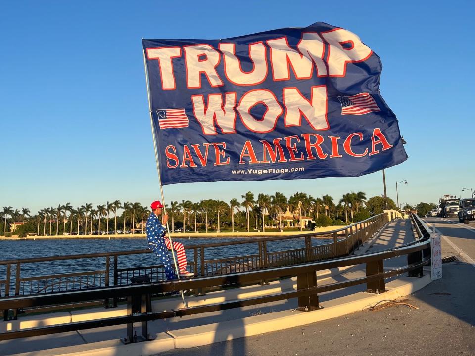 Trump supporter holds a pro-Trump flag, with Mar-a-Lago in the background.