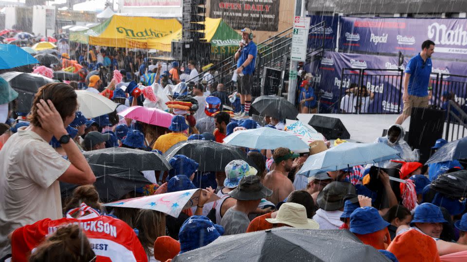 People take shelter from the rain Tuesday at the Nathan's hot dog eating contest. - Amr Alfiky/Reuters