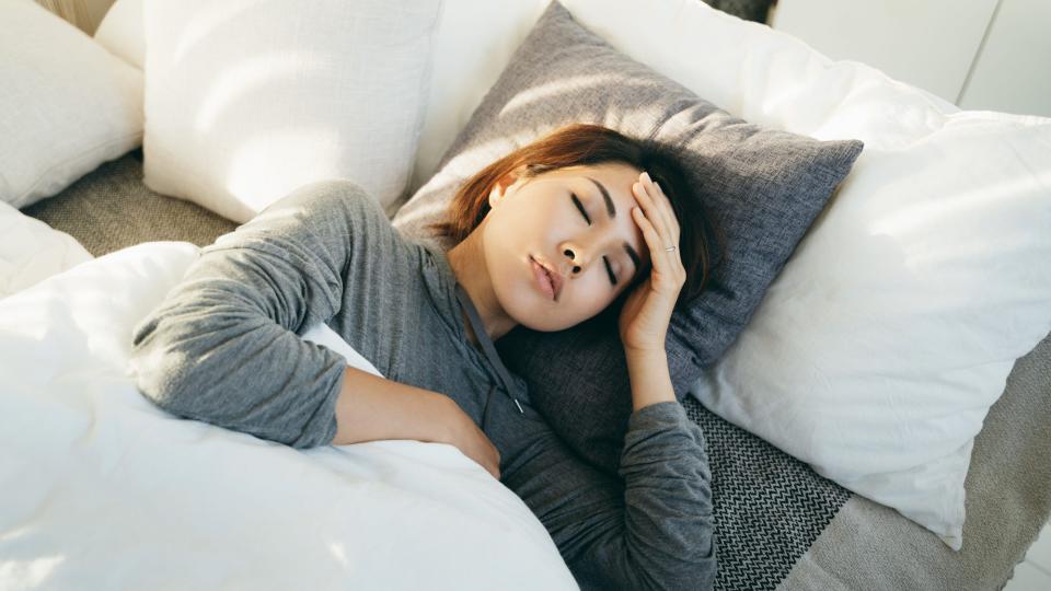 Young Asian woman with hand on forehead lying in bed