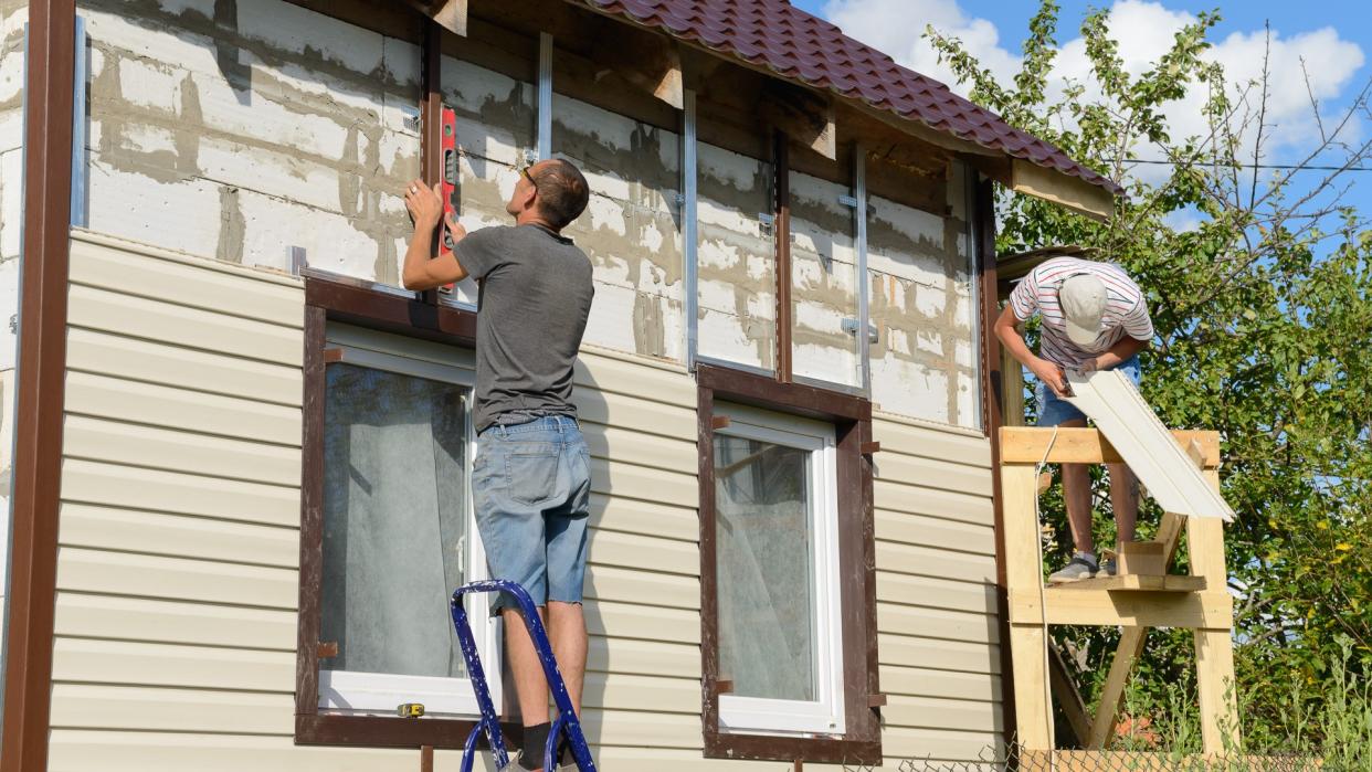 August 6, 2017: two workers polish the apartment building with vinyl siding.