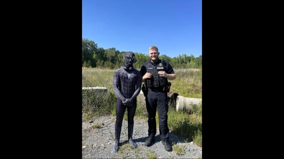 Patrol Officer Marshall Reece of the Waxhaw Police Department poses with a man seen walking on a road in a black Spider-Man costume.