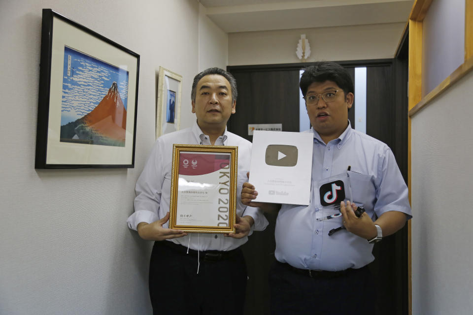 Daikyo Security Chief Executive Daisuke Sakurai, right, and General Manager Tomohiko Kojima hold the awards they have won recently for their Tik Tok videos in the hallway of their Tokyo headquarters office of Daikyo Security Co. in Tokyo Monday, Aug. 22, 2022. They’re your run-of-the-mill Japanese “salarymen,” but the chief executive and general manager at a tiny Japanese security company are among the nation’s biggest TikTok stars, drawing 2.7 million followers and 54 million likes, and honored with awards as a trend-setter on the video-sharing app. (AP Photo/Yuri Kageyama)