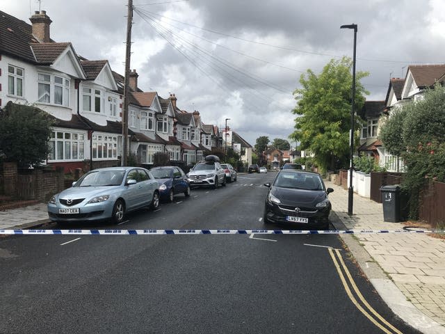 Police tape across a residential street, with cars parked on both sides.