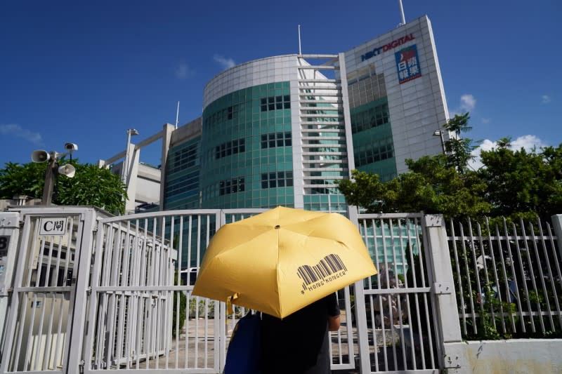 Supporter holding an umbrella stands in front of the entrance to the offices of Apple Daily and Next Media in Hong Kong