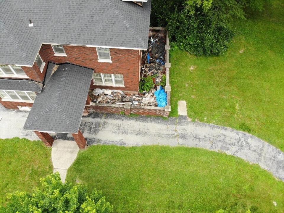 A drone photo shows a collapsed wrap-around porch at 8300 W. Main St. in Belleville. It’s filled with scrap wood, clay tiles from the old roof, other debris, weeds as tall as small trees and a blue tarp.