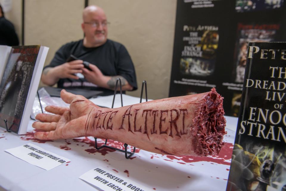 Local author Pete Altieri, who writes horror stories, uses a lifelike severed arm to attract attention to his booth at the five-year anniversary celebration of TAiLS of a Bookworm in Pekin. Twenty-four local authors gathered for book signings at the event.