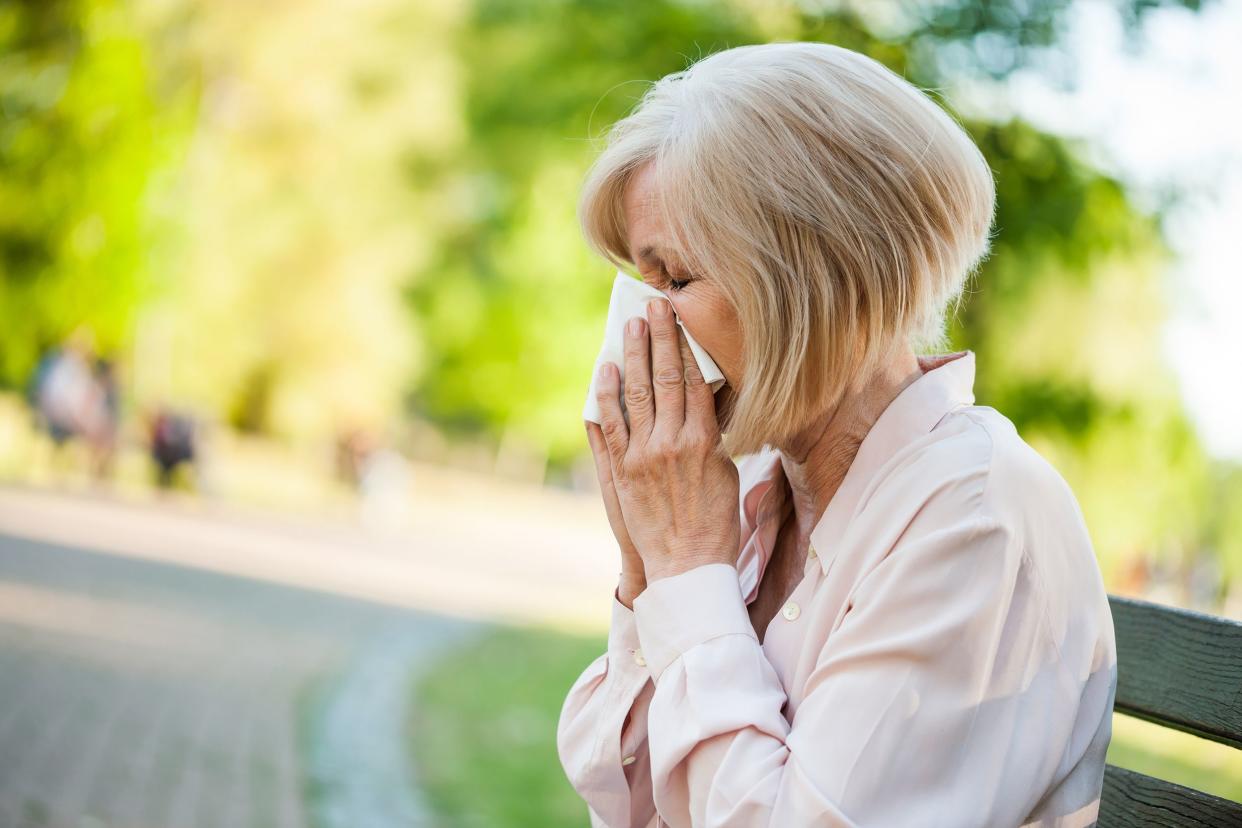 senior woman outside sitting on bench in park, blowing her nose