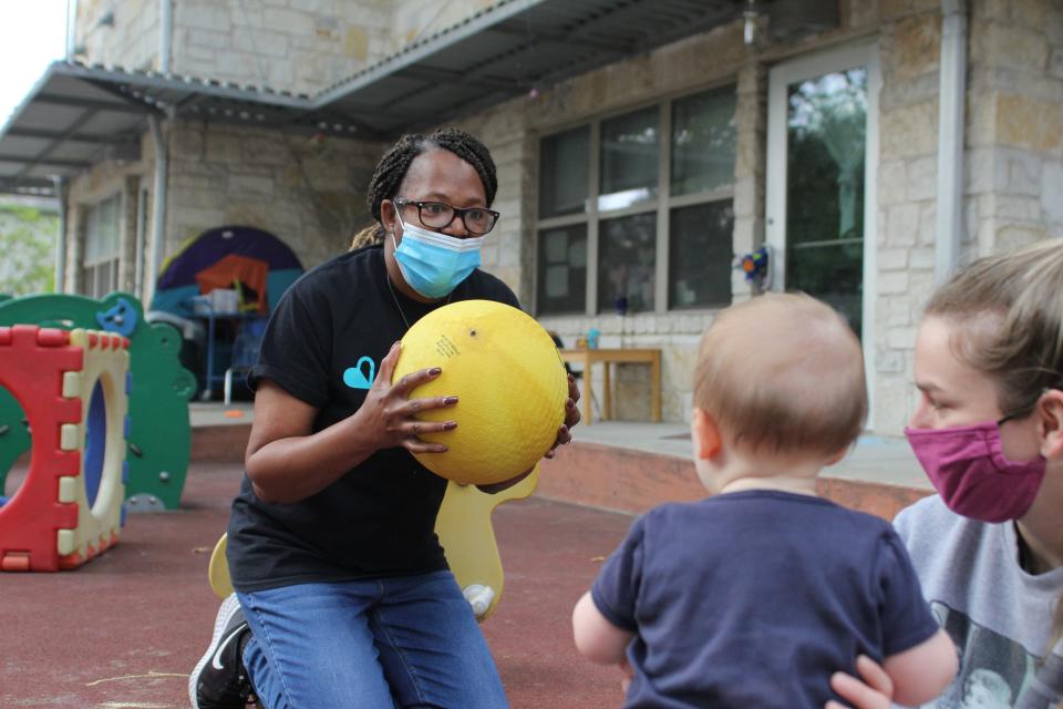 Sheila Matthews, the operations director at Open Door Preschools, plays with Kennedy Garris, an infant, on the playground at one of the school’s locations in Austin, Texas. The preschools are requiring the COVID-19 vaccine for staff, which has led to openings they can't fill.