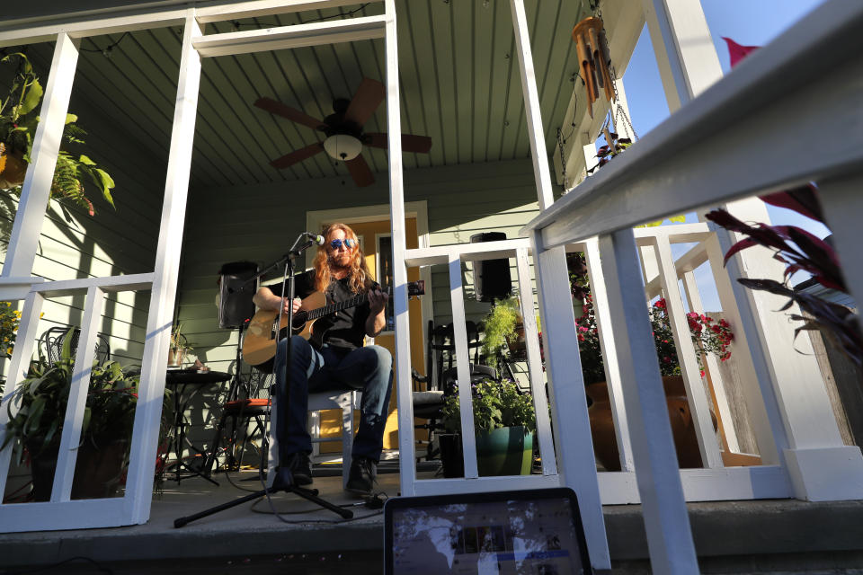 Adam Pearce performs a concert from his front porch in Jefferson Parish, La., a suburb of New Orleans, Wednesday, April 29, 2020. With New Orleans music venues shuttered for more than a month now because of the coronavirus outbreak, musicians and fans are finding new places to connect – porches, living rooms, studios and lawns – and reaching their largest audiences online, many streaming performances live on social media platforms. But for the city's club owners awaiting the green light to reopen there's concern about all the uncertainties, like how long it may take tourists to return, how soon the music scene will rebound and when it does, what it will look like. (AP Photo/Gerald Herbert)