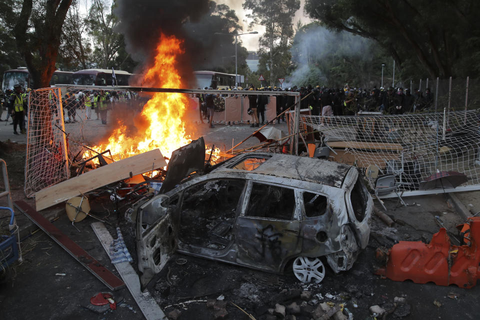 Students stand near a charred vehicle during a face-off with riot police at the Chinese University in Hong Kong, Tuesday, Nov. 12, 2019. Police fired tear gas at protesters who littered streets with bricks and disrupted morning commutes and lunch breaks Tuesday after an especially violent day in Hong Kong's five months of anti-government demonstrations. (AP Photo/Kin Cheung)