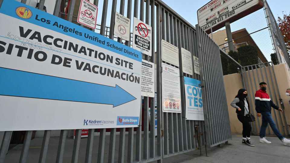 Two masked people walk out of a COVID-19 testing and vaccination site at a public school. 