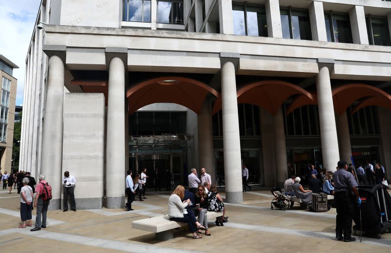 People stand and sit outside the London Stock Exchange in Paternoster Square, London