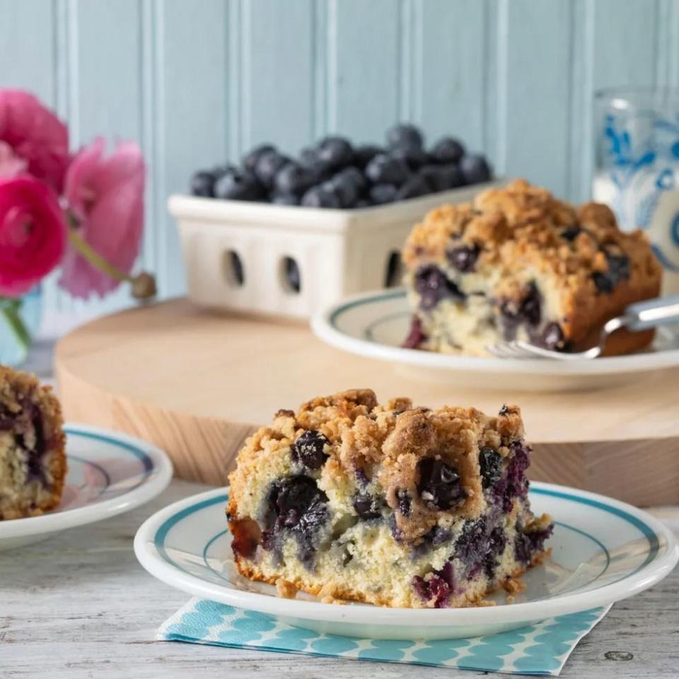 blueberry buckle coffee cake slice on plate with blueberry pint in back