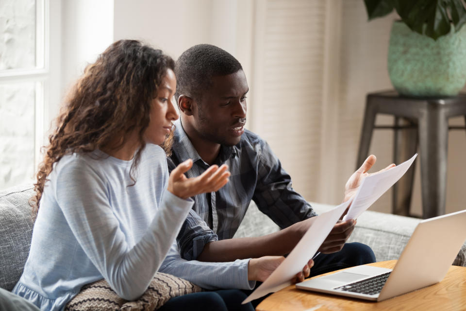 Concerned mixed race husband and wife take care of domestic bills reading papers at home, worried black couple consider bank documents, think of mortgage or loan, check paperwork together