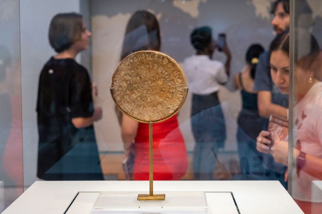 The Phaistos Disc, which is round and covered in glyphs, behind glass in a museum