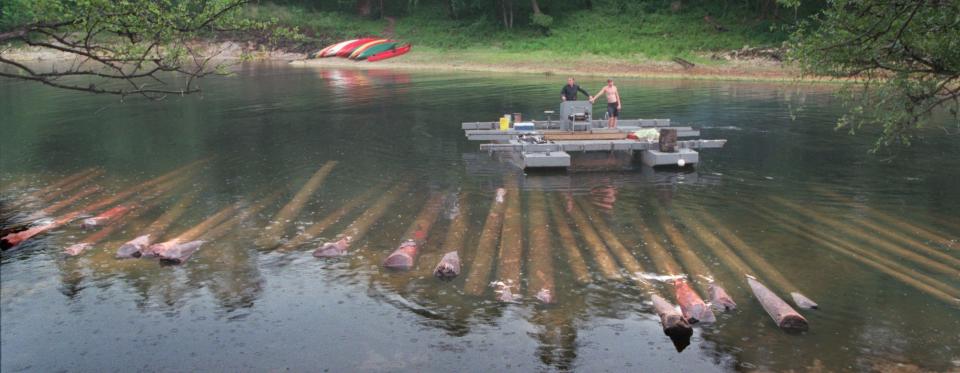 Fred Tatman, left, and his assistant Kirk Sadler maneuver a custom-designed pontoon barge past Longleaf pine logs that Tatman recovered from the bottom of the Suwannee River in 1999. The logs, most cut before the turn of the century, are stored along a shallow stretch of the Suwannee until they can be transported by truck to Goodwin Heart Pine Co. to be turned into heart pine lumber.