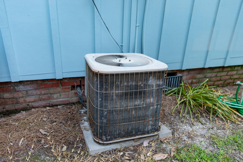 Old air conditioner system compressor next to home, needing maintenance.