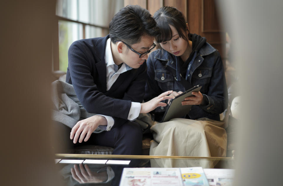 In this April 11, 2019, photo, engaged couple Kenzo Watanabe, left, and his fiancee Chiharu Yanagihara check a tablet device showing catalog of wedding dresses at a Japanese wedding company in Tokyo. Japan is getting ready for its biggest celebration in years with the advent of the Reiwa era of soon-to-be emperor Naruhito. That means big opportunities for businesses hoping consumers will splash out on long holidays and memorabilia. (AP Photo/Eugene Hoshiko)