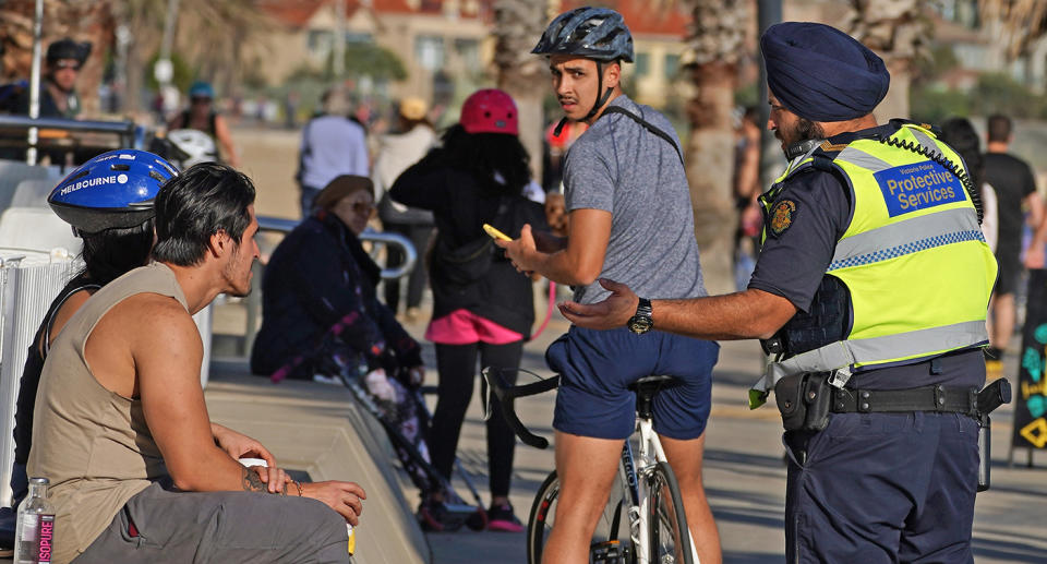 Victoria Police Protective Services Officers speak to a man at St Kilda beach in Melbourne, Monday, April 13, 2020. Victoria Police issued 433 fines between 11:00pm on Thursday and 11:00pm on Easter Sunday after conducting thousands of spot checks across the state. A shutdown of non-essential services is in effect Australia wide in a bid to slow the spread of the coronavirus (COVID-19) disease.(AAP Image/Scott Barbour) NO ARCHIVING