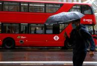 FILE PHOTO: A man with an umbrella walks past a bus in the City of London financial district during the morning rush hour